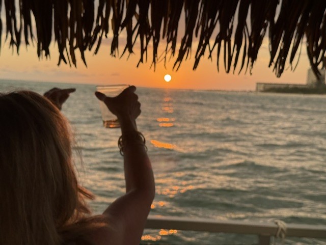 A guest raises a glass to the sunset aboard the Barefoot Tiki boat on Sarasota Bay